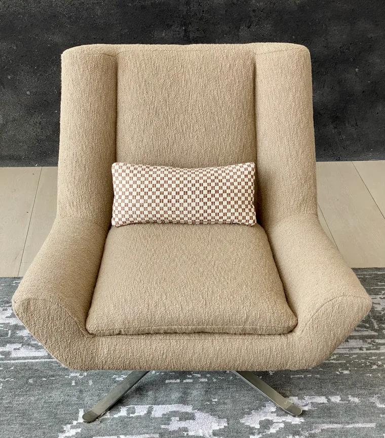 Swivel wing chair in tan boucle with a checkerboard pillow