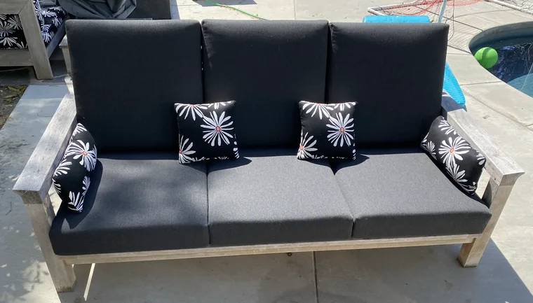 Teak outdoor sofa with charcoal cushions and print pillows